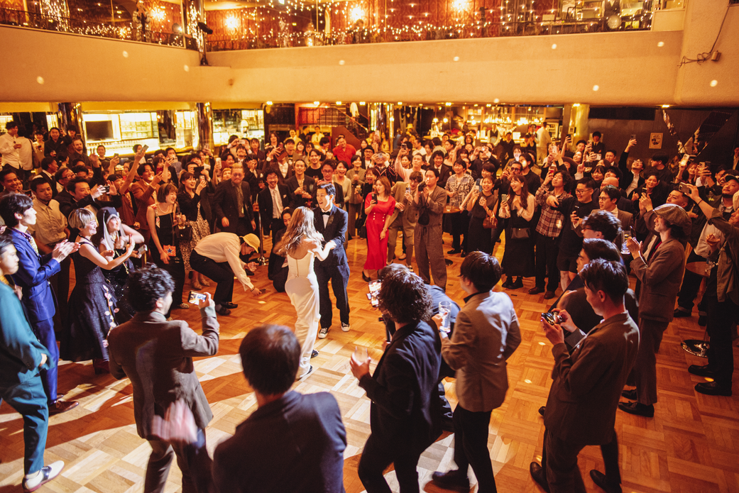 レトロなダンスホールで、80年代風の衣装に身を包んだ新郎新婦とゲストが友人バンドの生演奏で盛り上がっている祝祭のワンシーン