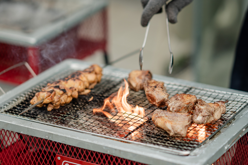 sasaのオープンキッチンで、シェフが薪火を使い豪快に肉を焼き上げているライブ感あふれる調理風景