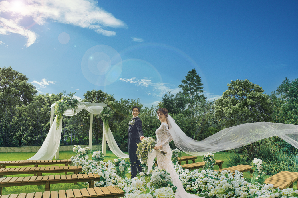 シェラトン鹿児島のガーデンチャペルで、青空と緑に囲まれて行われる挙式シーン。