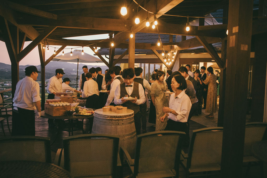 大きなケヤキの木の下で自由に行われるガーデンパーティー。ゲストがリラックスして会話や遊びを楽しみ、開放的な空気が漂う